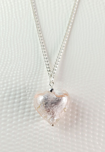 Ce collier comporte un pendentif en forme de coeur légèrement rosé tapissé de feuilles d'argent fabriqué par un artisan verrier et d'une chaîne plaquée argent maille gourmette. Ce collier est un bijou d'amour discret qui convient à tous les styles vestimentaires. Un cadeau idéal pour un être cher. Longueur de la chaîne : environ 50cm. Photo...