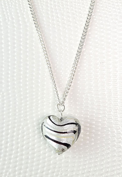 Coeur en verre soufflé et tapissé d'une feuille d'argent. Ce pendentif original à stries noires est accompagné d'une chaine plaquée argent de 45cm environ. Collier classique et original à la fois. Une idée de cadeau idéale pour témoigner de son amour. Bijou fantaisie.