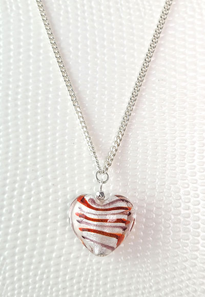 Collier composé d'un pendentif en forme de coeur tapissé de feuilles d'argent fabriqué par un artisan verrier et d'une chaîne plaquée argent maille gourmette. Ce collier est un bijou d'amour, le pendentif coeur comporte des stries rouge passion toutefois discrètes. Un cadeau idéal pour un être cher. Longueur de la chaîne : environ 50cm. Photo...